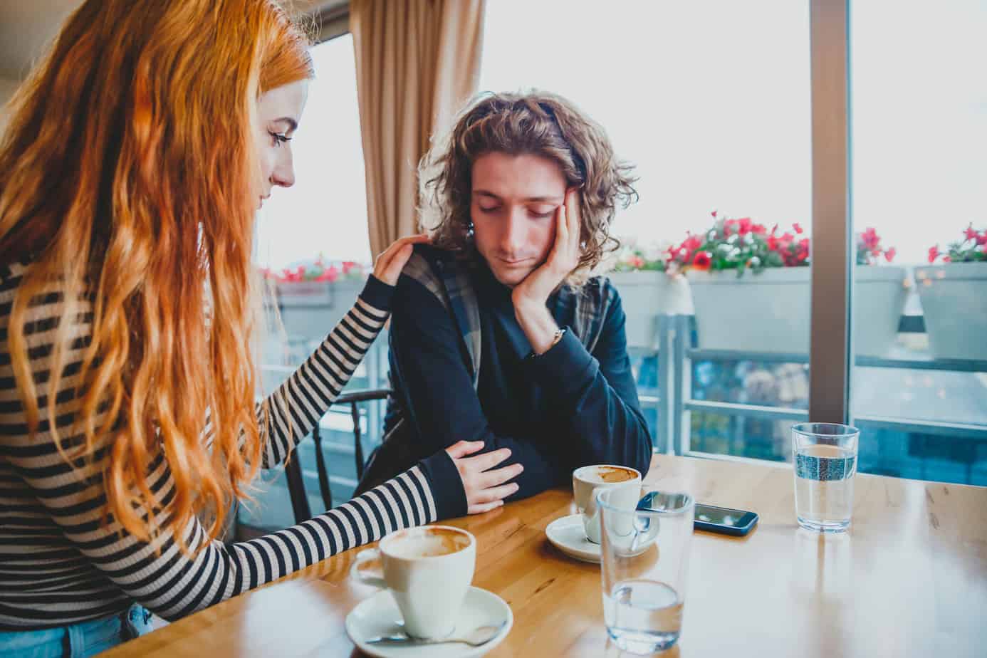 woman consoles sad man while enjoying coffee at table in restaurant