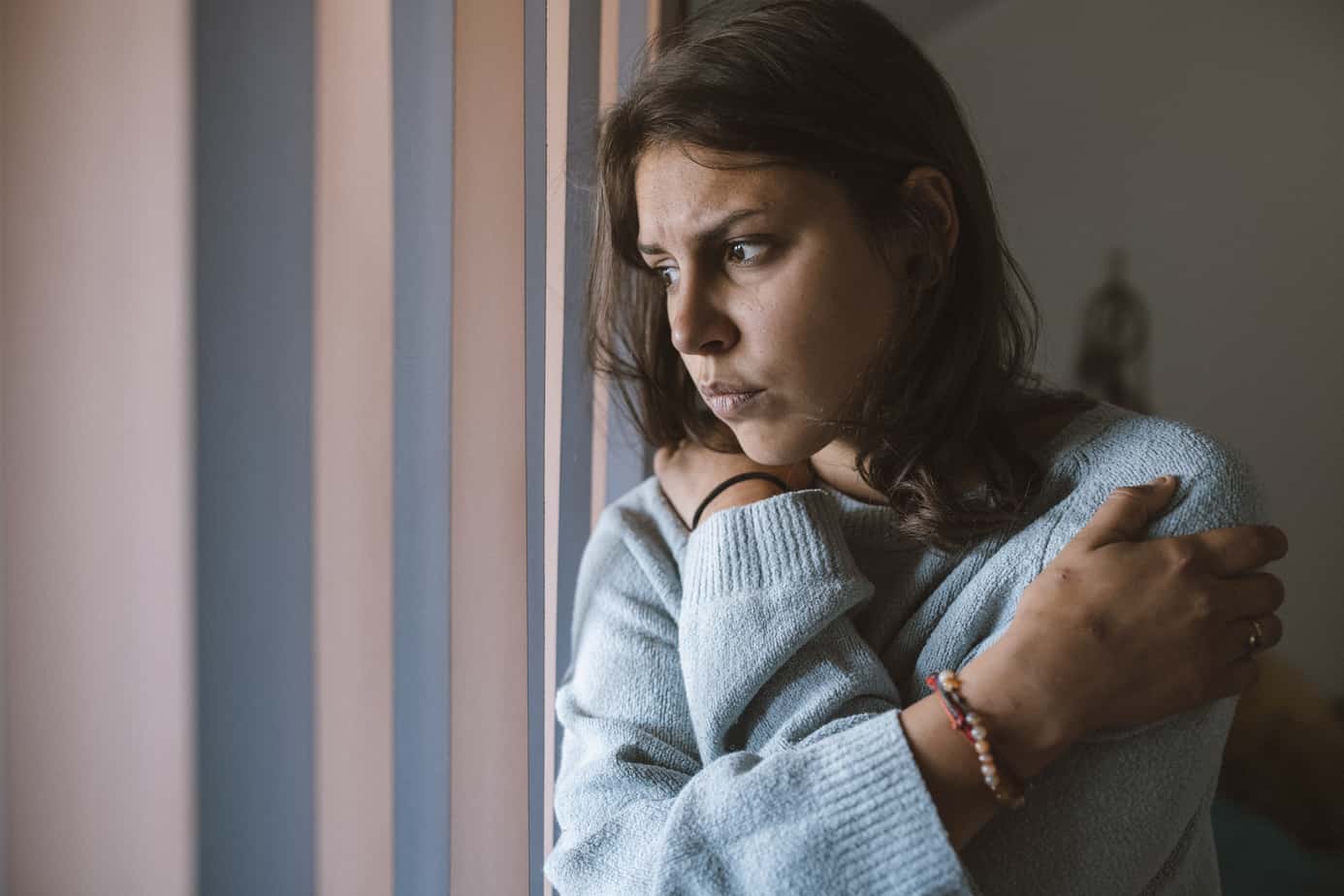scared woman standing next to window looking upset