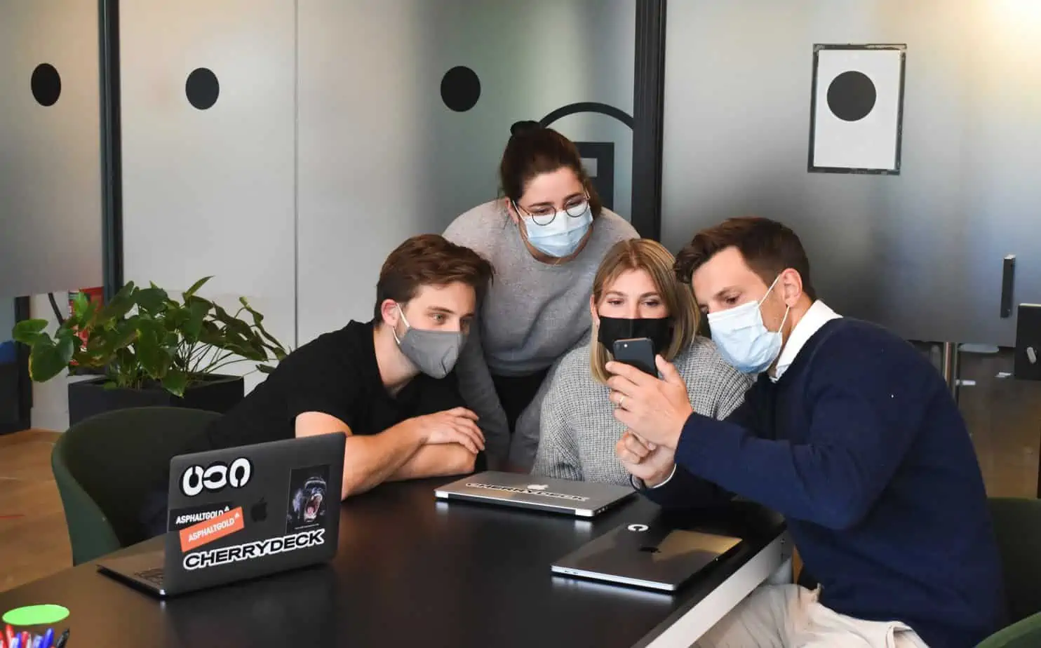 A group of coworkers in masks surround someone holding up a sample