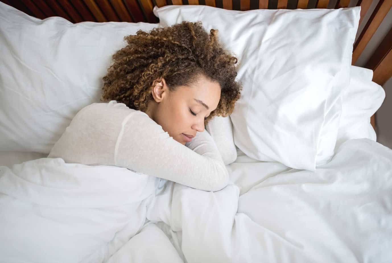 A woman asleep in bed with white linens at Mountainside's residency suite.