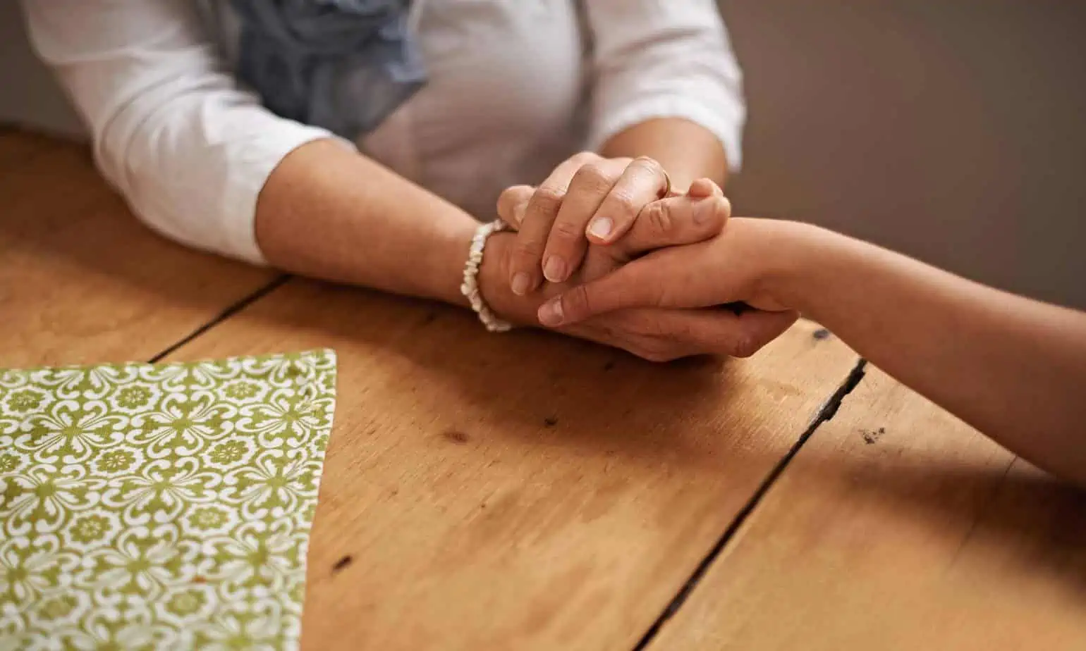 An older woman wearing a white shirt and bracelet holding a hand of a younger woman on table