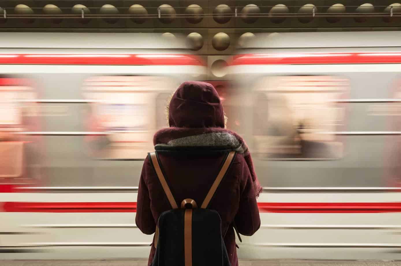 Back of person in red jacket and backpack waiting for fast moving train