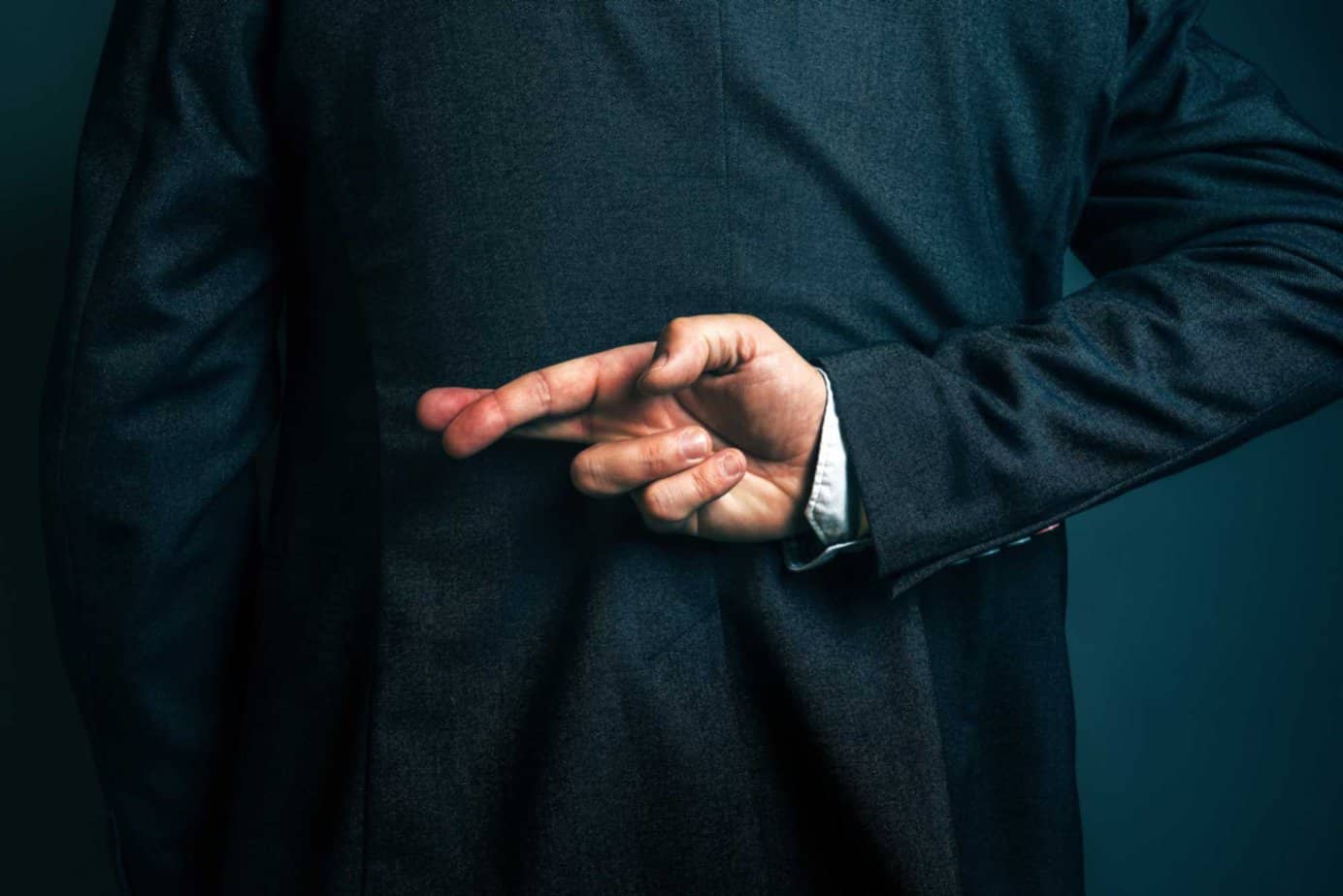 businessman crosses fingers secretly behind back, he's lying