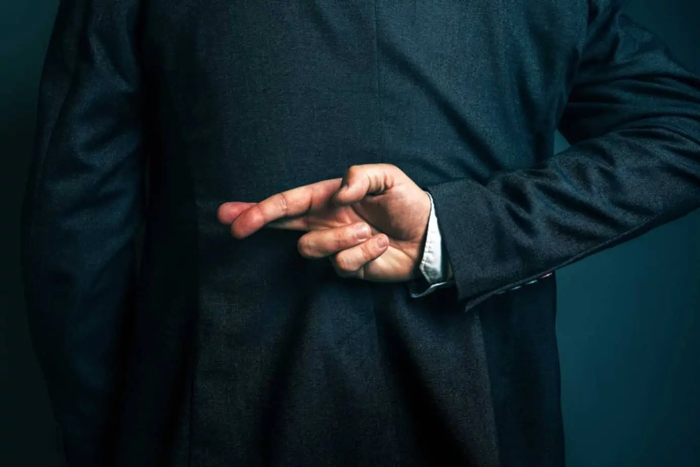businessman crosses fingers secretly behind back, he's lying