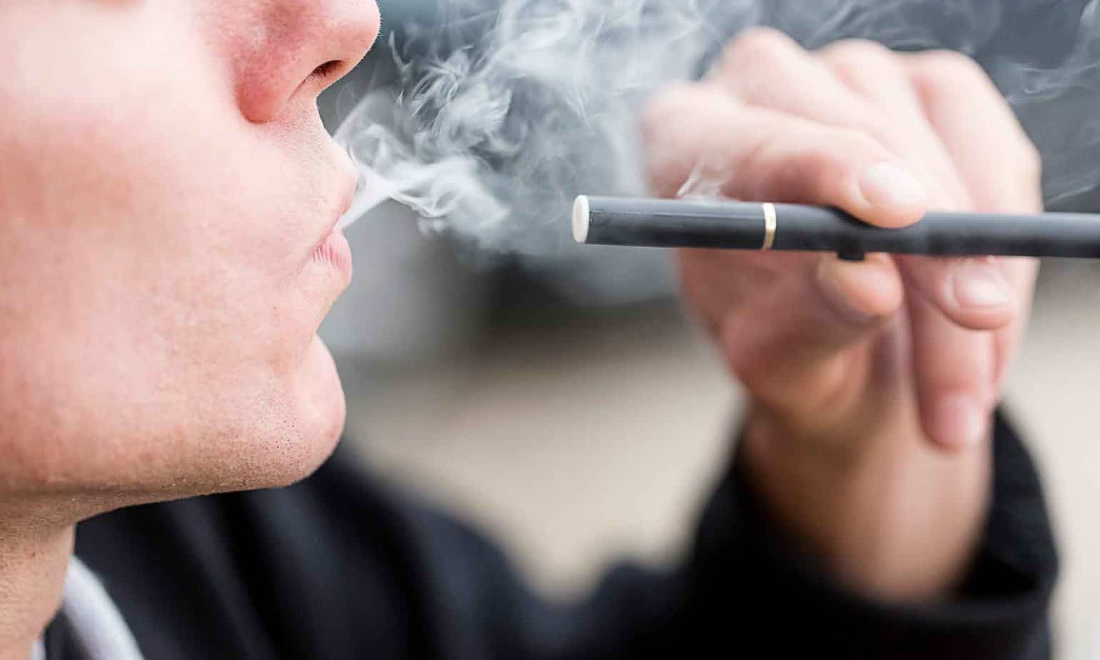 man smoking with ecigarette by his lips with smoke