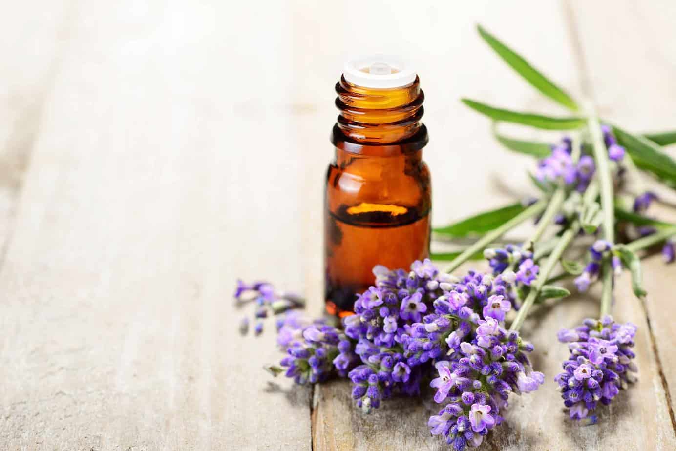 Essential oil vial with purple flowers on wooden table