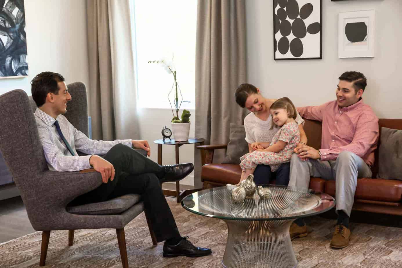Mom, dad, and young daughter sitting on a couch in a group counseling room during a family counseling session with a therapist