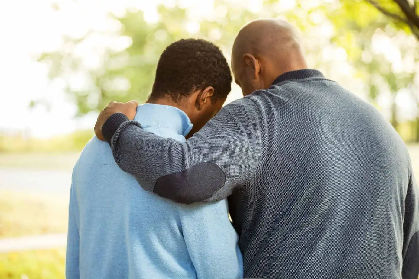 father holding shoulder of son while looking down outside by trees