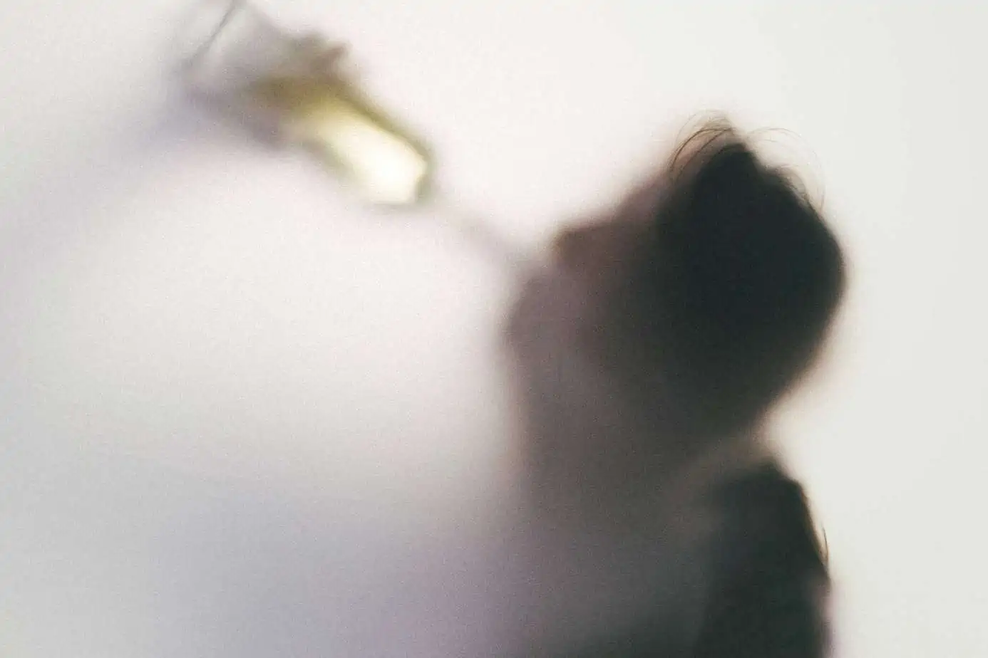 person drinking alcohol bottle behind fogged screen
