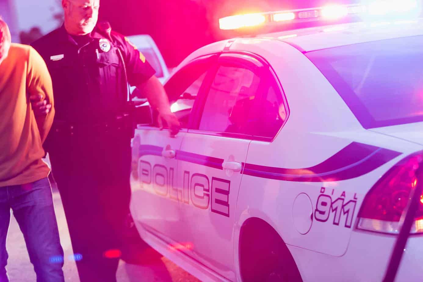 police officer arresting man next to police car with flashing lights