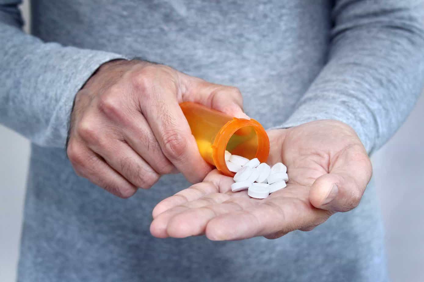 Man in gray shirt pouring prescription pills / drugs into hand