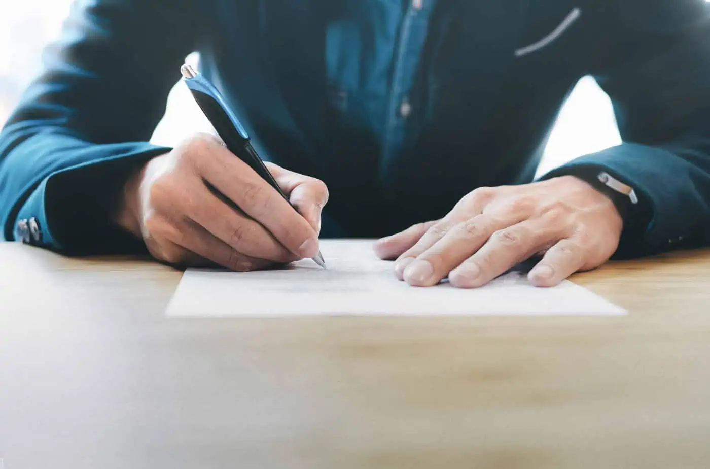close up of man in blue suit with hands writing a letter on a piece of paper with a pen