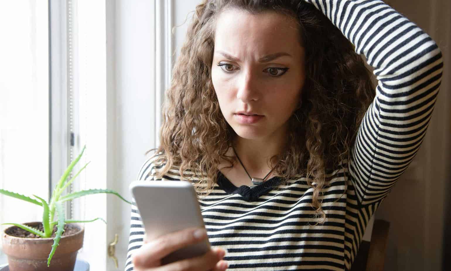 Woman looks alarmed and anxious while doomscrolling on her mobile phone