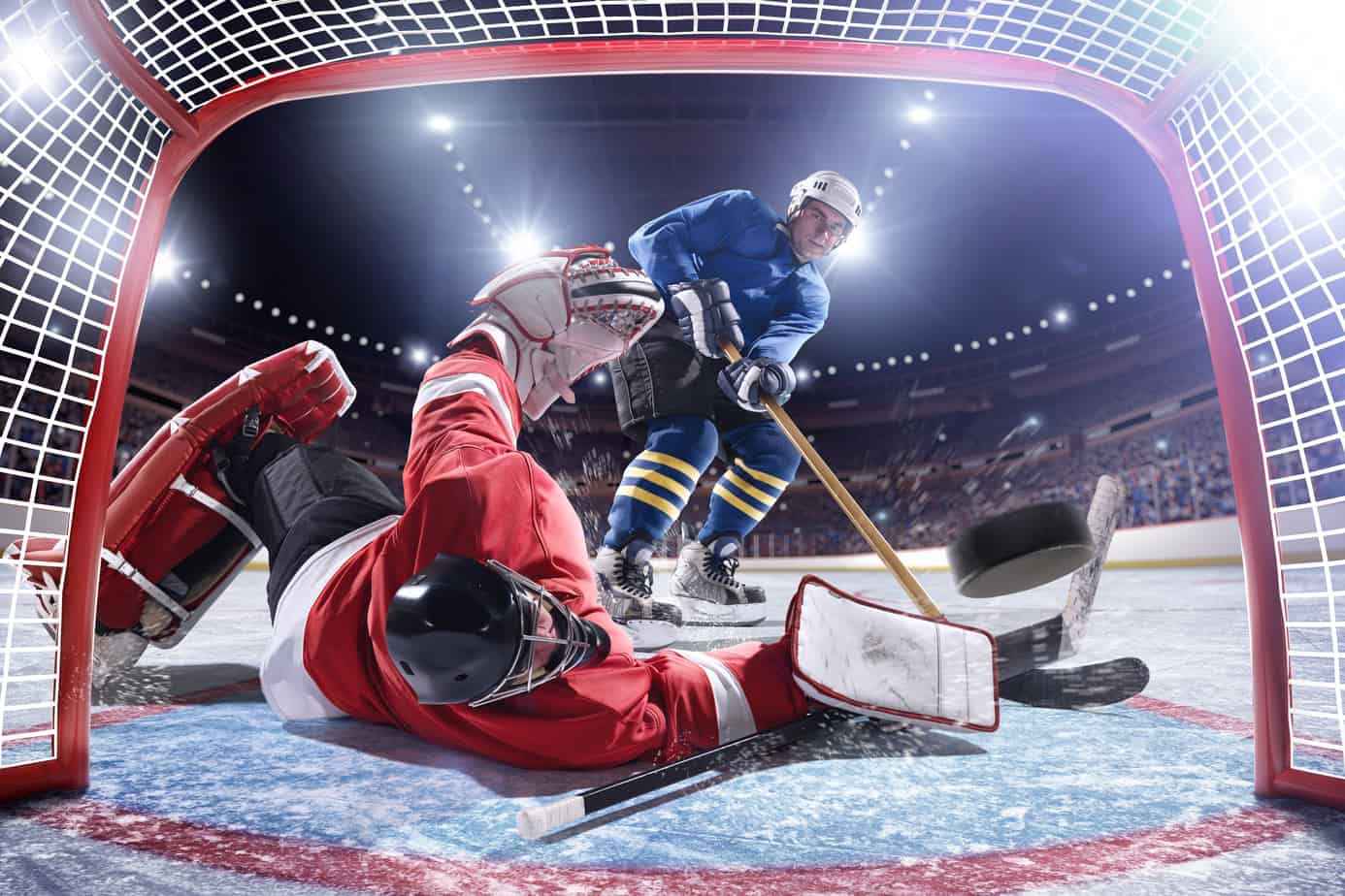 hockey player shooting puck into goal past fallen goalie