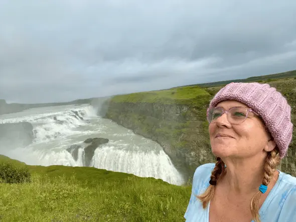 smiling woman poses in front of waterfall in field