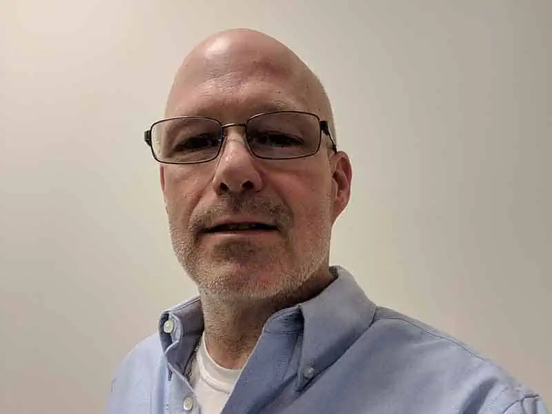 man in glasses poses in front of white background