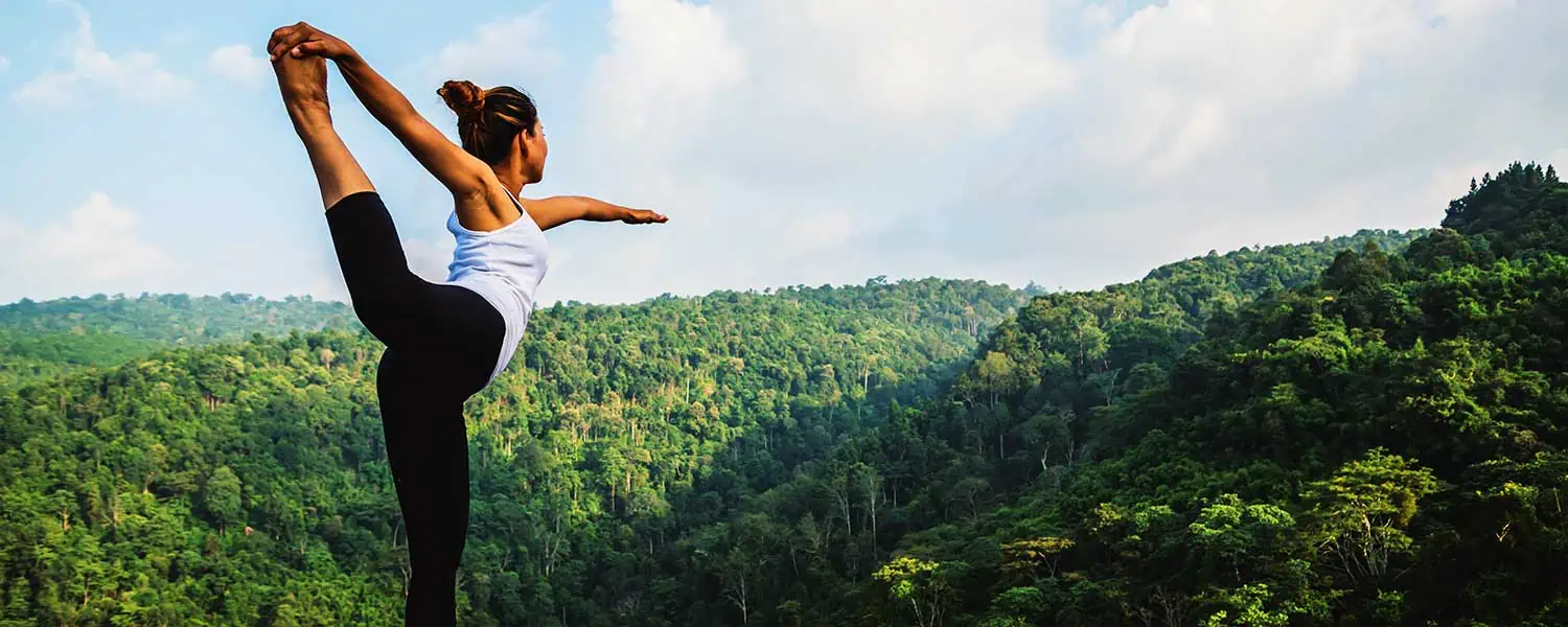 woman practicing yoga on a hill in a forested, hilly setting