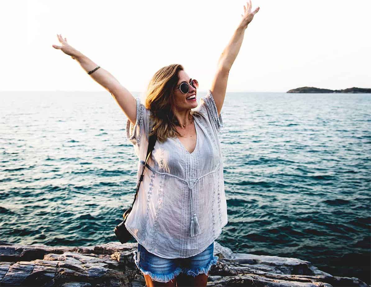 excited smiling woman with hands in the air by the water