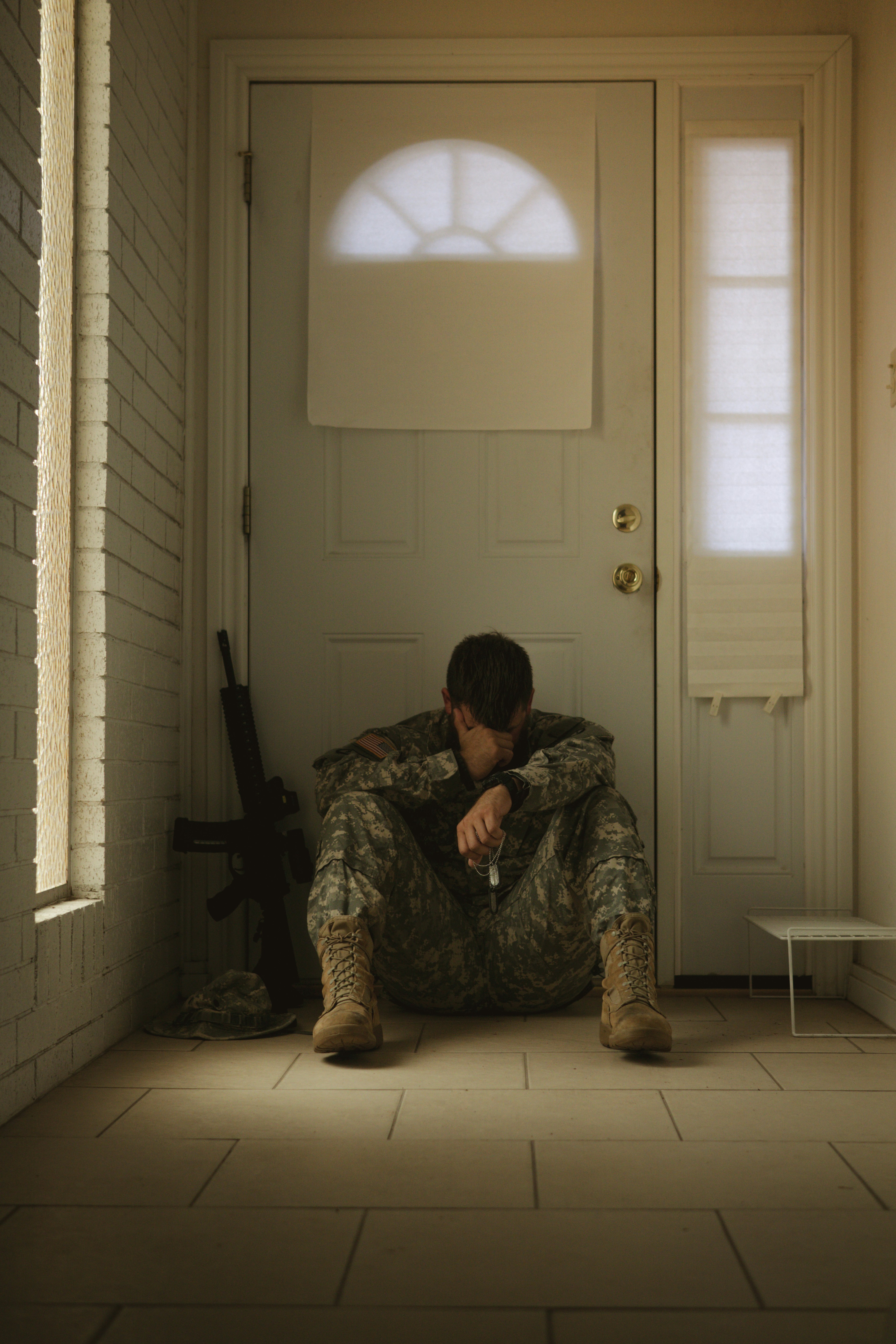 A veteran returns home and sits sadly inside his doorway experiencing mental health issues